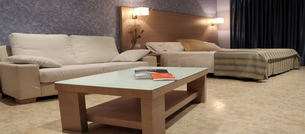 Habitación extra grande con una cama extra grande de 2 metros x 2 metros. Sofá de dos plazas y mesa de centro.
